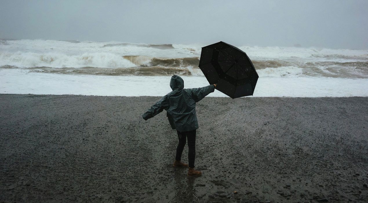 Person on a beach in stormy weather, holding an umbrella that's caught in the wind