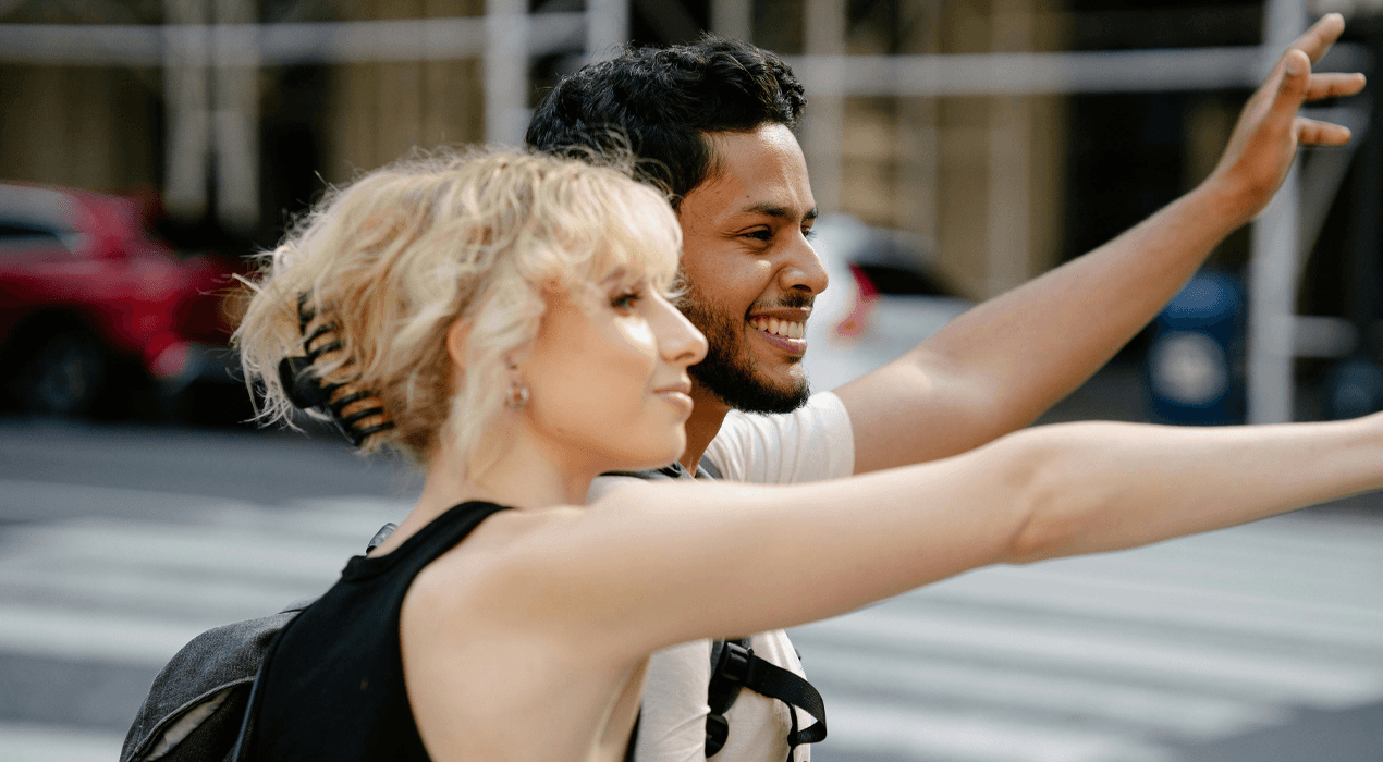 Close up of a young man and woman standing on the side of the road flagging down a bus or taxi
