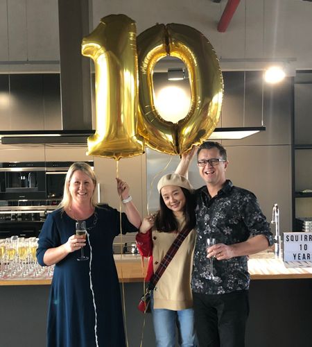 Three people standing holding up '10' balloons