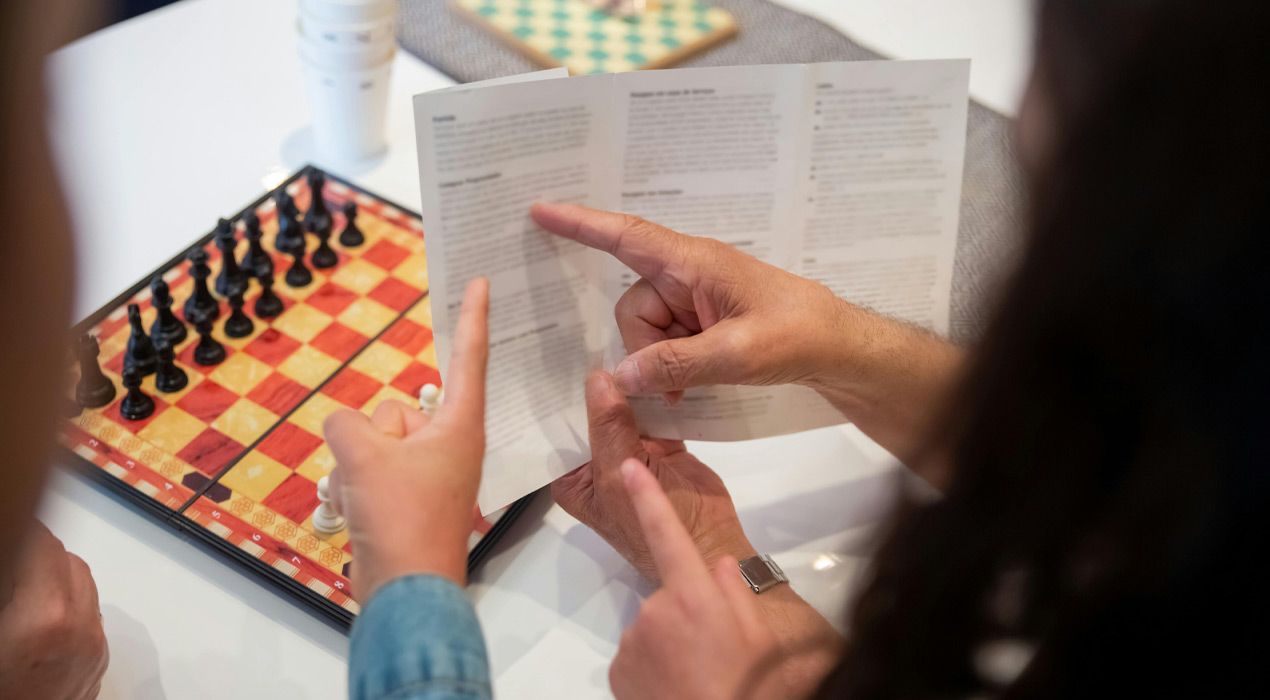 Two people sitting at a table about to play chess, reading the rules