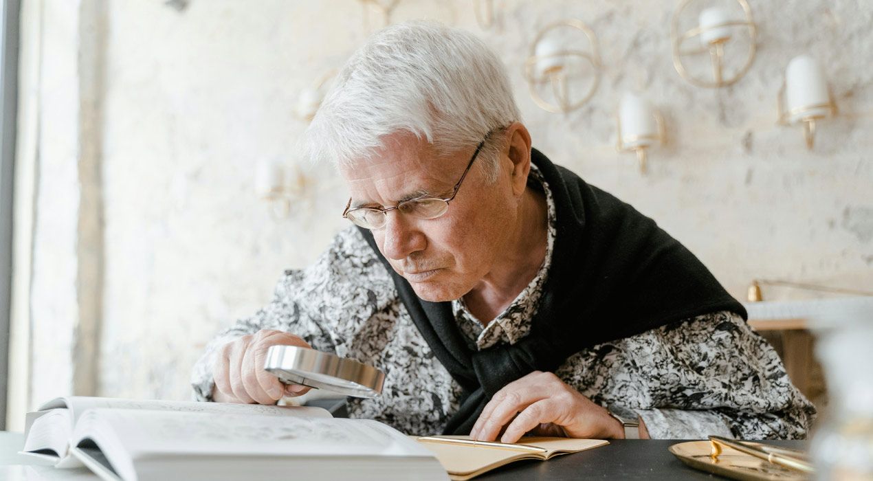 Older man reading a book using a magnifying glass