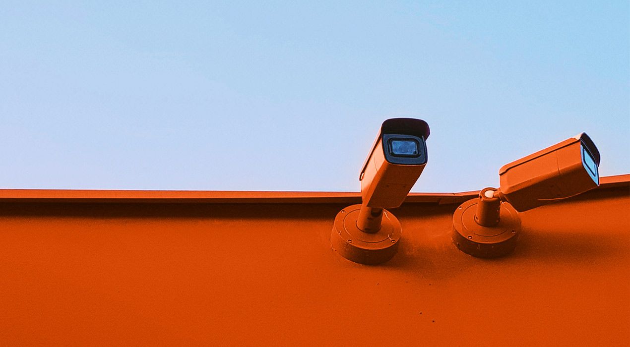 Two security cameras installed on an external wall of a building, with blue sky in the background