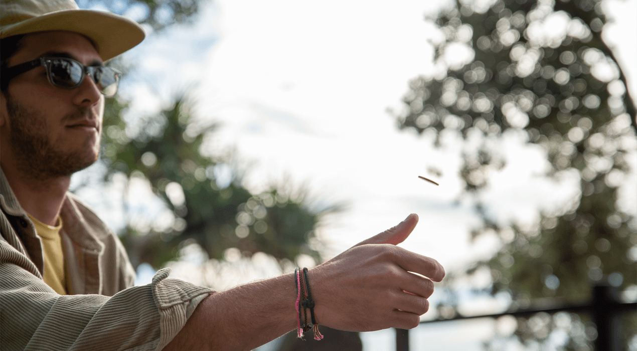 Man flipping a coin, sitting outside with trees in the background