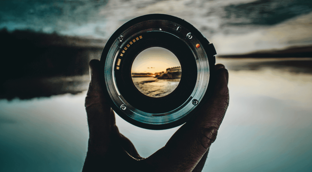 Hand holding a camera lens through focused on a landscape background