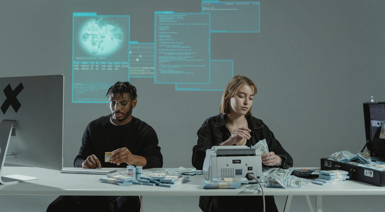 A man on a computer and a woman counting cash, with hacker-type graphics in the background