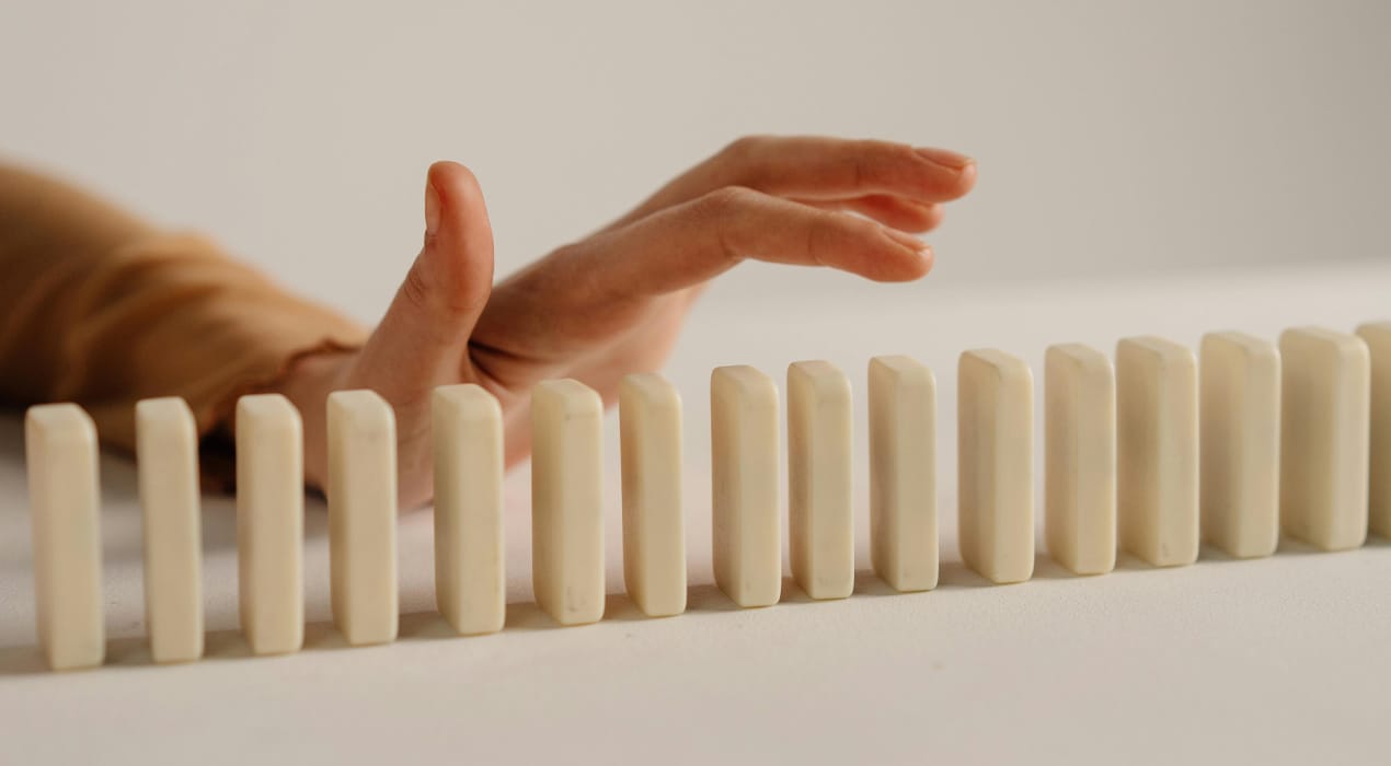 Row of dominoes laid out in a line, with a hand hovering over them as if about to knock them over