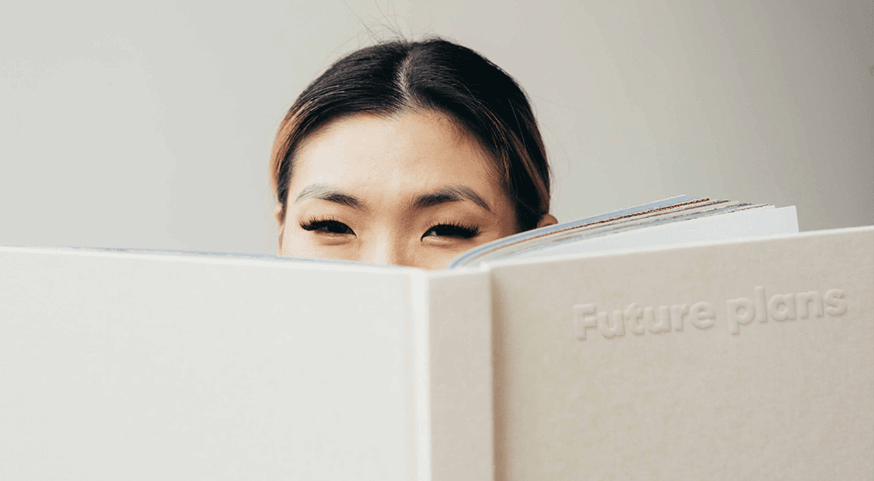 Woman peering over the top of a large open book with a white cover, titled "Future Plans"