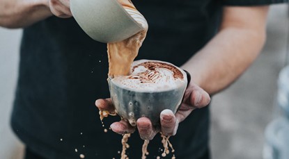 Person pouring cup of coffee into another cup, overflowing