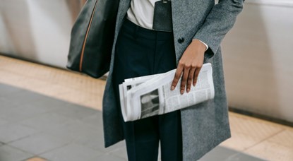 Woman in work attire carrying newspaper and a bag
