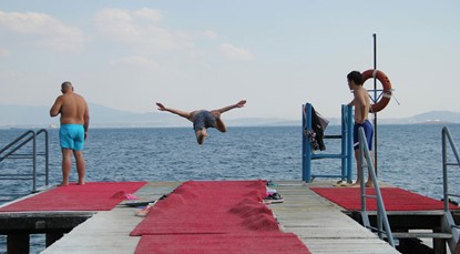 Two men watching as another jumps off a platform into the ocean