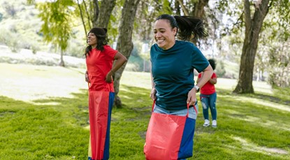 Pair of young women taking part in a sack race in a park