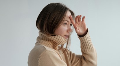 Young woman pictured from the shoulders up, wiping one finger across her forehead in a show of relief