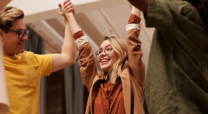 Group of young people standing together holding hands, lifting their arms up in the air in celebration