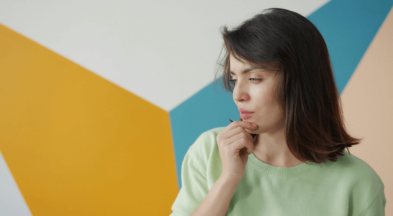 Woman standing against a colourful wall with her hand to her chin deep in though