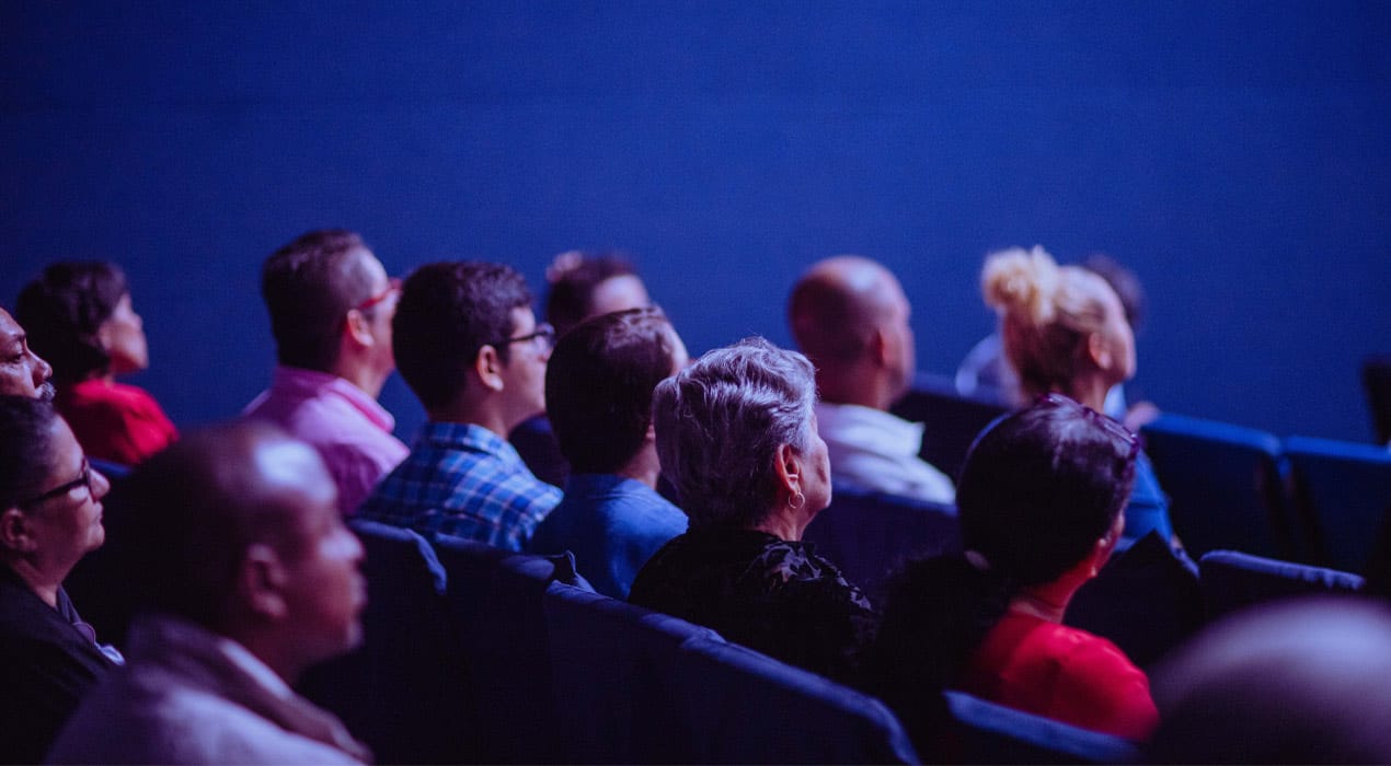 Group of people sitting in a theatre or cinema, looking ahead.
